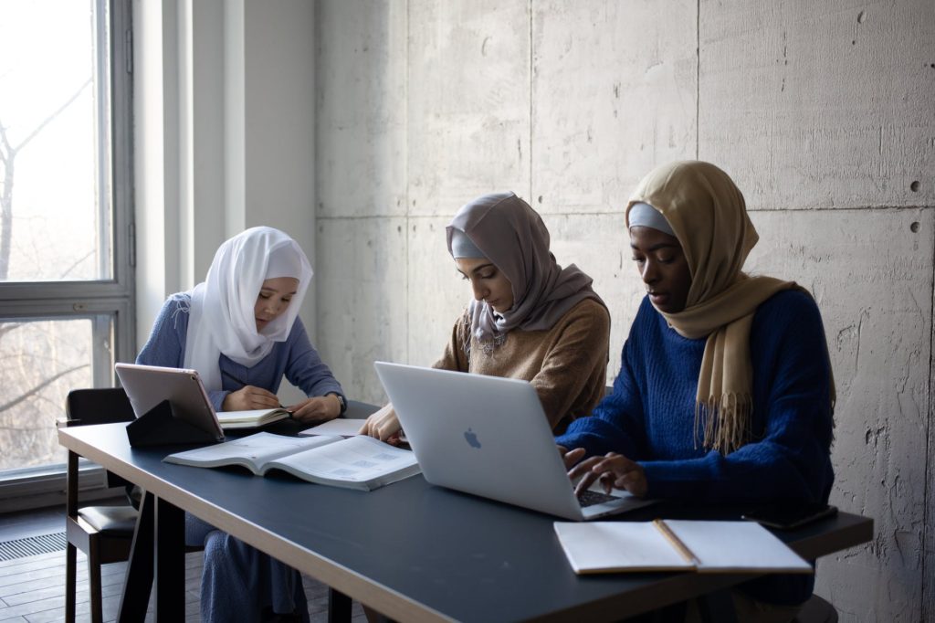 multiracial muslim ladies in hijab using laptops and notebooks